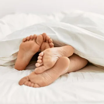 A Couples Feet Under Sheets On a bed at home.