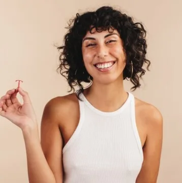 Young woman smiling at the camera while holding an IUD in her hand