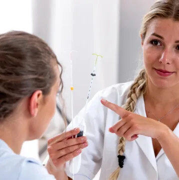 A healthcare professional showing intrauterine devices (IUDs), including the Mirena Coil, to a patient during a medical consultation.
