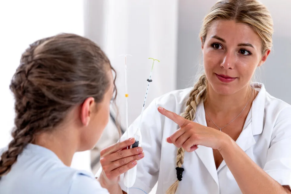 A healthcare professional showing intrauterine devices (IUDs), including the Mirena Coil, to a patient during a medical consultation.