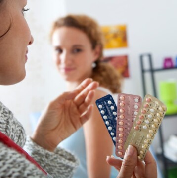 A healthcare professional shows different packs of birth control pills, including the Progestogen-Only Pill, to a patient in a medical office and explains possible side effects such as desogestrel bleeding.