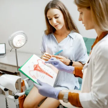 Doctor showing a picture with uterus to a young woman patient, explaining the features of women's health during a medical consultation in the office