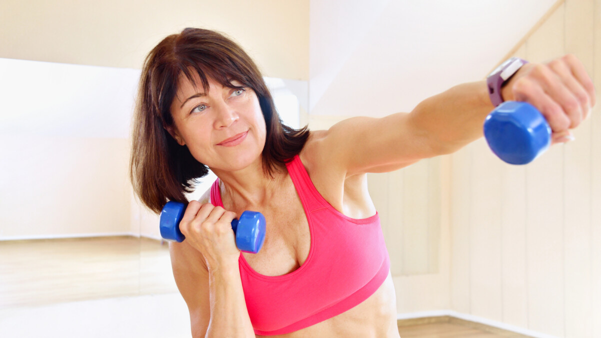 A woman in athletic wear exercises indoors, holding blue dumbbells and extending one arm forward in a punching motion—an example of staying active and strong through exercise during perimenopause.